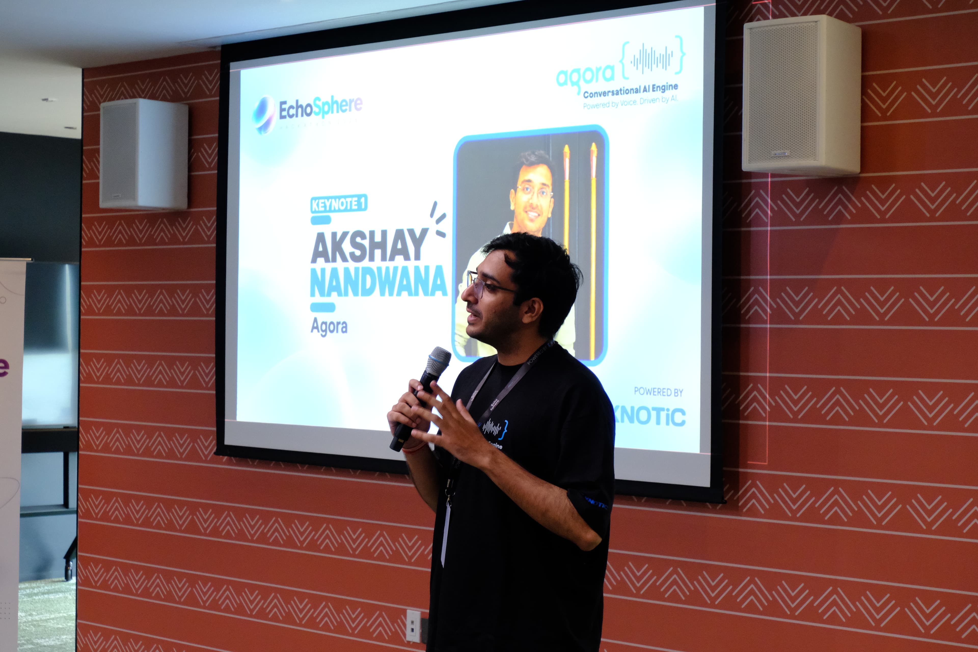 Akshay speaking into a microphone in front of an EchoSphere keynote slide